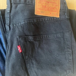 Svarta Levi's 501 jeans W28 L32 - Klassiska svarta Levi's 501 jeans med rak passform och fem fickor. Jeansen har den ikoniska läderpatchen bak i midjan och röd Levi's-tagg på bakfickan. Tillverkade i kraftigt jeanstyg som ger en tidlös look.