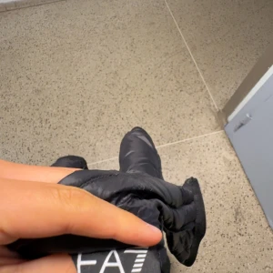 Svart dunväst från EA7 Emporio Armani - Säljer en svart dunväst från EA7 Emporio Armani med quiltad design och dragkedja framtill. Västen har en stilren look med logga på bröstet och är perfekt för lager-på-lager. Lätt och smidig att bära, passar till många outfits. Pris kan diskuteras vid snabb affär,västen är i nyskick använd 1-3 gånger 