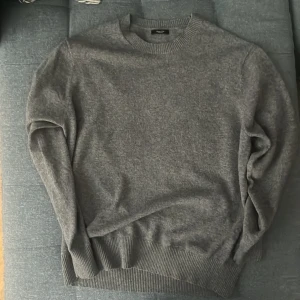 Grå stickad tröja från Massimo Dutti - Mysig grå stickad tröja från Massimo Dutti med rund halsringning och ribbade muddar. Perfekt för lager-på-lager och chill dagar. Enkel och stilren design som funkar till det mesta. Snygg att matcha med jeans eller chinos. Nypris 549 säljer för 150 storlek M