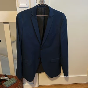 Blå super slim kavaj Jack & Jones - Mörkblå kavaj från Jack & Jones Premium i super slim fit. Klassisk modell med två knappar framtill, fickor med lock och bröstficka. Snyggt fodrad insida och stilren look som passar perfekt till skjorta och smala byxor.storlek 50 skulle gissa är typ M