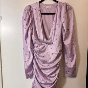 Ljuslila blommig klänning från Adoore - Supersöt ljuslila kortklänning från Adoore med små blommor, djup v-ringning och långa puffärmar. 