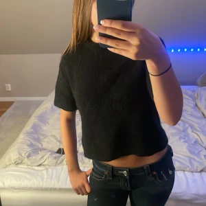 Svart stickad topp från Gina Tricot - En svart, croppad stickad topp från Gina Tricot med korta ärmar och enkel design. Toppen har en rak passform och är tillverkad i ett mjukt stickat material som känns skönt mot huden. Perfekt att styla med jeans eller kjol för en clean look.