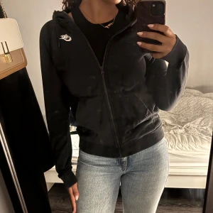 Svart hoodie från Nike - Säljer en svart hoodie från Nike med dragkedja och huva. Den har en klassisk design med Nike-logga på bröstet och praktiska fickor framtill. Perfekt för en avslappnad stil.