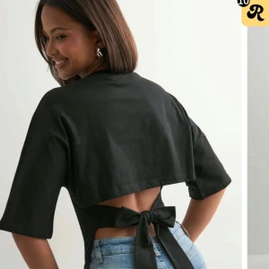 Svart bolerotopp med knyt från Nelly - Svart bolerotopp från Nelly med halvlånga ärmar och snygg öppen rygg som knyts med en stor rosett baktill. Toppen har en croppad passform och är gjord i mjukt bomullstyg. Perfekt för dig som vill ha en stilren men ändå unik look.