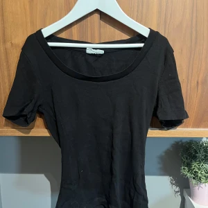 Svart ribbad topp med kort ärm - En svart, tight ribbad topp med korta ärmar och rundad halsringning. Enkel och stilren modell som är lätt att matcha med olika outfits. Perfekt för dig som gillar en basic look med en snygg passform.