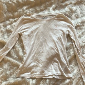 Vit långärmad Ralph Lauren - Klassisk vit långärmad tröja från Polo Ralph Lauren i mjuk bomull. Tröjan har rund halsringning och en liten broderad logga i ljusrosa på bröstet. Perfekt basic-plagg med clean look och skön passform. (Osäker på ifall jag vill sälja så priset diskuteras ej)