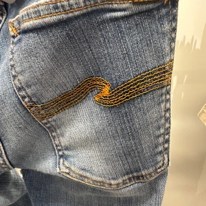 Blå skinny jeans från Nudie Jeans - Snygga blå skinny jeans från Nudie Jeans med klassisk orange söm och ikonisk brodyr på bakfickan. Jeansen har normal midja, fem fickor och är tillverkade i stretchig bomullsmix för en bekväm passform.