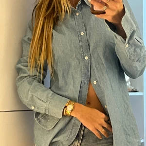 Ljusblå skjorta från Filippa K - Säljer en stilren ljusblå skjorta från Filippa K i bomull. Skjortan har klassisk krage, vita knappar framtill och på ärmsluten samt lång ärm. Perfekt för en clean och avslappnad look, lätt att matcha med jeans eller kjol.