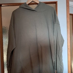 Grön hoodie  - Olivgrön hoodie i bomull med klassisk huva och snörning på sidan. Tröjan har långa ärmar med muddar och en relaxed, loose passform. 