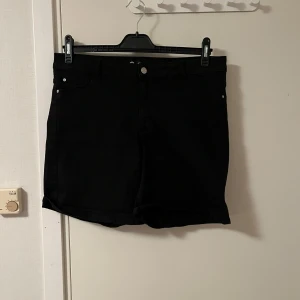 Svarta jeansshorts Jane XL - Svarta jeansshorts från Jane i storlek XL. Klassisk femficksmodell med knapp och dragkedja framtill. Snygg och enkel design som passar till allt, perfekt för varma dagar. Materialet är jeans och shortsen har en normal passform.Katt finns i hemmet 