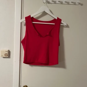 Röd croppad linnetopp från SHEIN - Snygg röd croppad linnetopp från SHEIN i 100% polyester. Toppen har breda axelband och v-ringad hals, perfekt för att lyfta vilken outfit som helst. Enkel och stilren design som passar dig som gillar färg och vill sticka ut. Katt finns i hemmet 