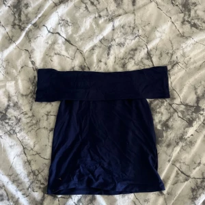 Marinblå offshoulder topp Kappahl - Snygg marinblå offshoulder topp från Kappahl. Modellen är axelbandslös och har en bred kant upptill som ger en trendig look. Perfekt att styla med jeans eller kjol för en cool vibe.