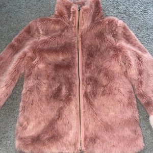 Rosa pälsjacka med dragkedja - Fluffig och supermjuk rosa pälsjacka med hel dragkedja framtill och hög krage. Jackan har långa ärmar med ljusare rosa detaljer vid ärmsluten. Perfekt för dig som vill sticka ut och hålla dig varm under kyliga dagar.