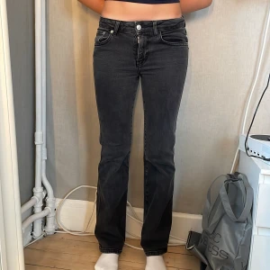 Grå bootcut jeans från 157 - Snygga grå jeans från 157 med bootcut-modell och klassisk 90-talsvibe. Jeansen har fem fickor, coola bakfickor med lock och silverfärgade knappar. Tillverkade i mjukt denimtyg med dragkedja och knapp framtill. Perfekta för en avslappnad och trendig look.