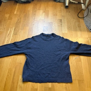Mörkblå stickad tröja från 157 - Mysig mörkblå stickad tröja från 157 i storlek XS. Tröjan har en klassisk rund halsringning och långa ärmar. Perfekt för lager-på-lager och chill dagar. Materialet känns mjukt och har en lätt textur som ger en avslappnad vibe.