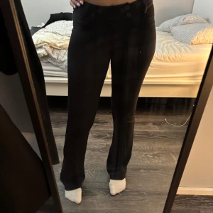 Svarta bootcut byxor Gina Tricot - Snygga svarta byxor från Gina Tricot i bootcut-modell. Byxorna har låg midja, två knappar framtill och sitter tajt över låren men släpper ut vid bensluten. Perfekta för dig som gillar en klassisk och stilren look.