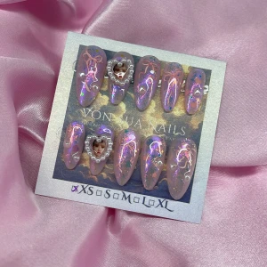 SwiftHeart (XS);Medium Almond - Handgjorda press-on naglar i en medium mandelform med skimrande rosa bas, iriserande glitter, små hjärtan, pärldekor och söta rosa rosetter. Naglar har två 3D-pärlram i hjärtform. Perfekt för dig som vill ha unika och kreativa naglar, och älskar Taylor Swift! I storlek XS: 14 mm, 11 mm, 11,5 mm, 10 mm, 8 mm  