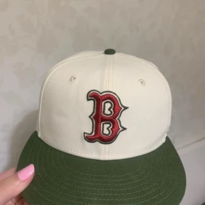 Beige och grön keps  - Säljer en beige keps från New Era med grön skärm och broderad röd B-logga framtill. På sidan finns 'World Series 1986'-brodyr och MLB-logga bak. Helt oanvänd