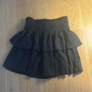 Svart volangkjol med resårmidja - Supersöt svart kortkjol med bred smockresår i midjan och dubbla volanger som ger en riktigt snygg och fluffig look. 