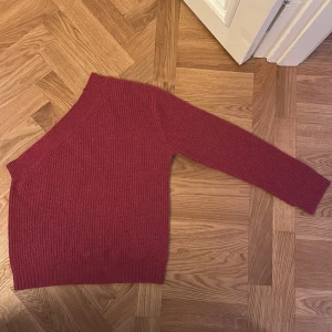 Vinröd one shoulder kashmirtröja Soft Goat - Säljer en vinröd ribbstickad tröja från Soft Goat i 100% kashmir. Tröjan har en snygg one shoulder-design och lång ärm på ena sidan. Strl M (passar S-M). 