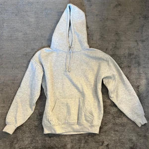 Ljusgrå hoodie från Bikbok - Enkel och stilren ljusgrå hoodie med huva och snörning. Tröjan har en stor magficka framtill och ribbade muddar vid ärmslut och nederkant. Perfekt för chill dagar eller när du vill ha något bekvämt och avslappnat. Hoodien har två små blå färgfläckar. Inga övriga slitningar.