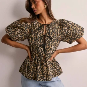 Leopardmönstrad blus från Nelly - Supersnygg blus från Nelly med leopardmönster i beige och svart. Modellen har puffiga korta ärmar, volang nertill och snygg snörning framtill. Perfekt för dig som vill sticka ut med ett djurmönstrat statement-plagg.
