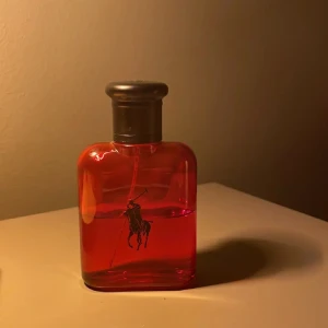 Ralph Lauren Polo Red parfym - En snygg parfymflaska från Ralph Lauren Polo Red med ikonisk svart polospelare på framsidan. Flaskan är i klarrött glas med rundade kanter och har ett mörkgrått lock. Perfekt för dig som gillar stilrena och sportiga dofter.skriv om ni undrar något!