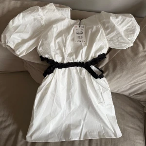 Vit kortklänning med puffärm och svart detalj - Superfin vit kortklänning med puffiga korta ärmar och svart rynkad detalj i midjan. Klänningen är helt oanvänd. Den är från Zaras barnavdelning och är i storlek 156💗