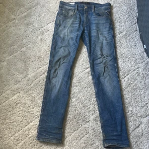 Replay anbass med slitningar - Säljer ett par klassiska blå jeans från Replay med snyggt slitna detaljer och raka ben. Jeansen har fem fickor, normal midja och är tillverkade i mjukt bomullstyg. Perfekta för dig som gillar en avslappnad men stilren look. De är ganska slim, hör av dig vid minsta fundering😊