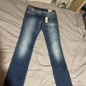 Lågmidjade blå jeans - Snygga blå jeans från Diesel, modell NewZ, med klassisk femficksdesign och diskret slitning framtill och baktill. Jeansen har raka ben och normal passform, samt coola detaljer på bakfickorna. Perfekta för dig som gillar en stilren och avslappnad look. Jeansen är helt nya men prislappen kvar