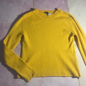 Gul ribbad tröja från Divided - Gul långärmad tröja från Divided i ribbad bomull. Tröjan har en rund halsringning och smal passform som sitter snyggt på kroppen. Perfekt för att liva upp din outfit med en poppig färg. Storlek S.