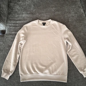 Beige sweatshirt från H&M Relaxed Fit - En stilren beige sweatshirt från H&M i relaxed fit. Tröjan har rund halsringning, långa ärmar och ribbade muddar. Tillverkad i en mjuk blandning av bomull och polyester som känns skön mot huden. Perfekt för en chill och enkel look.