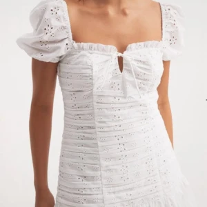 Vit kort klänning med puffärm och broderi - Superfin vit kort klänning med puffärmar, broderade blommor och söt knytning framtill. 