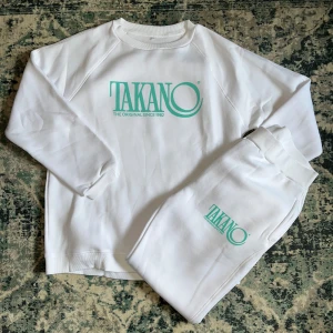 Vita mjukisbyxor och sweatshirt från Takano - Säljer ett set med par vita mjukisbyxor från Takano med grönt tryck på ena benet och en sweatshirt med trycket på också. Byxorna har resår i midjan, är mjuka inut och har rak passform även vid benslutet. 