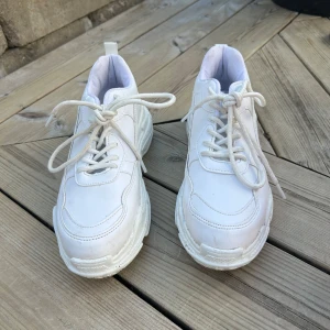 Vita chunky sneakers - Säljer ett par vita chunky sneakers med snörning och platt sula. Skorna har en sportig och modern design med rund tå och tjock yttersula. Perfekta för dig som gillar en stilren och trendig look.