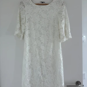 Vit spetsklänning med trekvartsärm - Superfin vit klänning i spets med trekvartsärmar och rund halsringning. Klänningen har ett romantiskt blommönster och är perfekt för somriga tillfällen eller student. Lätt och luftig känsla med vackra spetsdetaljer. Använt en gång. 