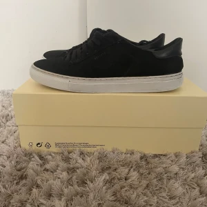 Axel Arigato Clean 90 – Black Suede - Axel Arigato Clean 90 – Black Suede Storlek: 42 Nypris: ca 2499 kr  Säljer ett par Axel Arigato Clean 90 i svart mocka – stilrena sneakers i premiumkvalitet. Klassisk siluett med lyxig känsla, tillverkade i italiensk mocka med vit gummisula och guldfolierad logga.  Skick: Knappt använda – mycket fint skick Endast minimala tecken på användning Levereras med originalkartong  Perfekta för både vardag och dressade tillfällen. Passa på att fynda ett par ikoniska Arigato till sommaren.