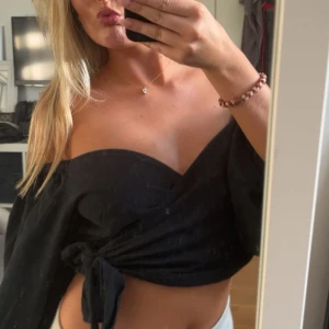 Svart omlottopp med puffärm - Köp via instabox!!! Snygg svart omlottopp med puffiga ärmar och knyt i midjan. Djup v-ringning framtill och croppad modell.