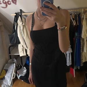 Svart klänning med korsade band  från Calvin Klein - Säljer en svart klänning från Calvin Klein med korsade axelband med CK-logga. Öppen rygg och är perfekt för en trendig och stilren look.