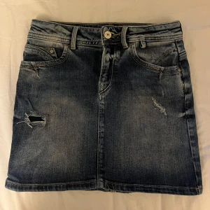 Blå jeanskjol  - Säljer en skitsnygg blå jeanskjol från LTB med slitna detaljer. Strl 158 vilket jag skulle säga motsvarar storlek xs/s beroende lite på. (Har vikt upp kjolen på 3e bilden)