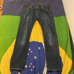Mörkblå raka jeans - Säljer ett par klassiska mörkblå jeans från J.Lindberg med raka ben och kontrastsömmar. Jeansen har fem fickor, gylf med dragkedja och knapp samt diskreta slitningar framtill. Passar perfekt till vardags och har en tidlös look.