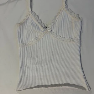 Sommar linne - Säljer en jätte  söt vit ribbad topp med spets längst kanterna. Toppen har en liten rosett framtill och är perfekt för sommaren. Materialet är mjukt och stretchigt💕.