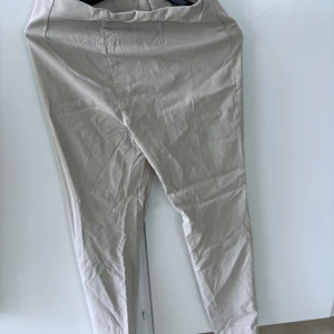 Beige byxor från Flash Woman - Säljer ett par beige byxor från Flash Woman i storlek S. Byxorna har en enkel och stilren design med hög midja och smal passform. Perfekta att matcha med en snygg topp eller stickad tröja.