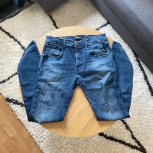 Klassiska blåa Replay jeans - Tja👋 Säljer ett par klassiska blå jeans från Replay med fem fickor och snygga slitningar framtill👖 Byxorna har normal passform och raka ben. Märkespatch bak i midjan och silverfärgade knappar och dragkedja🧷 Byxorna är i Anbass modell och har hyperflex material! Storleken på byxorna är W32 L32📐 Kom privat för mått!📏  Priset är INTE ristat i sten så kom gärna med prisförslag!💵  Vid frågor: Meddela oss!📩