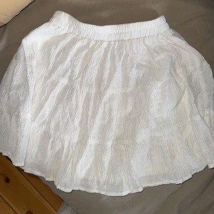 Vit volangkjol med resår i midjan - Säljer en söt vit kjol med volanger och resår i midjan. Kjolen är kort och har en luftig känsla, perfekt för varmare dagar. Passar till många olika stilar och är lätt att matcha med olika toppar.