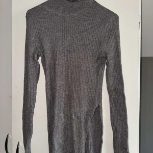 Grå ribbad tröja - Säljer en grå ribbad tröja med lång ärm. Tröjan har en smal passform och slittat nertill. Den har dock ett hål i vänster arm.