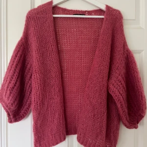 Rosa stickad kofta - Säljer en fluffig rosa stickad kofta med lös passform och 3/4 ärmar. Perfekt att slänga över en topp för en mysig och trendig look. Koftan är öppen framtill och har en luftig struktur. Nypris: 700kr