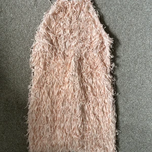 Ljusrosa fjäderklänning - Säljer en supercool ljusrosa klänning täckt med fjäderliknande detaljer. Klänningen är ärmlös och har en rak, kort passform som ger en riktigt trendig look. Perfekt för dig som vill sticka ut på festen! Den är öppen i ryggen med halterneck!