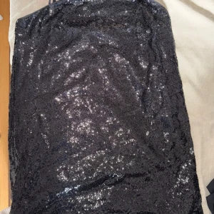Svart paljettklänning med smala axelband - Säljer en svart glittrig klänning med smala axelband och rak halsringning. Klänningen är täckt av paljetter som ger en snygg och festlig look. Perfekt för dig som vill sticka ut med en elegant och trendig stil.