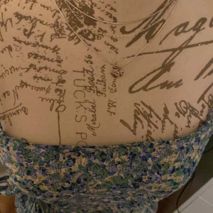 Blommig sommarklänning från Vero Moda - Söt blommig klänning från Vero Moda i blå, grön och vit med knyt i midjan. Klänningen är ärmlös och har en luftig passform, perfekt för varma dagar. Lätt material och volangdetalj nertill.